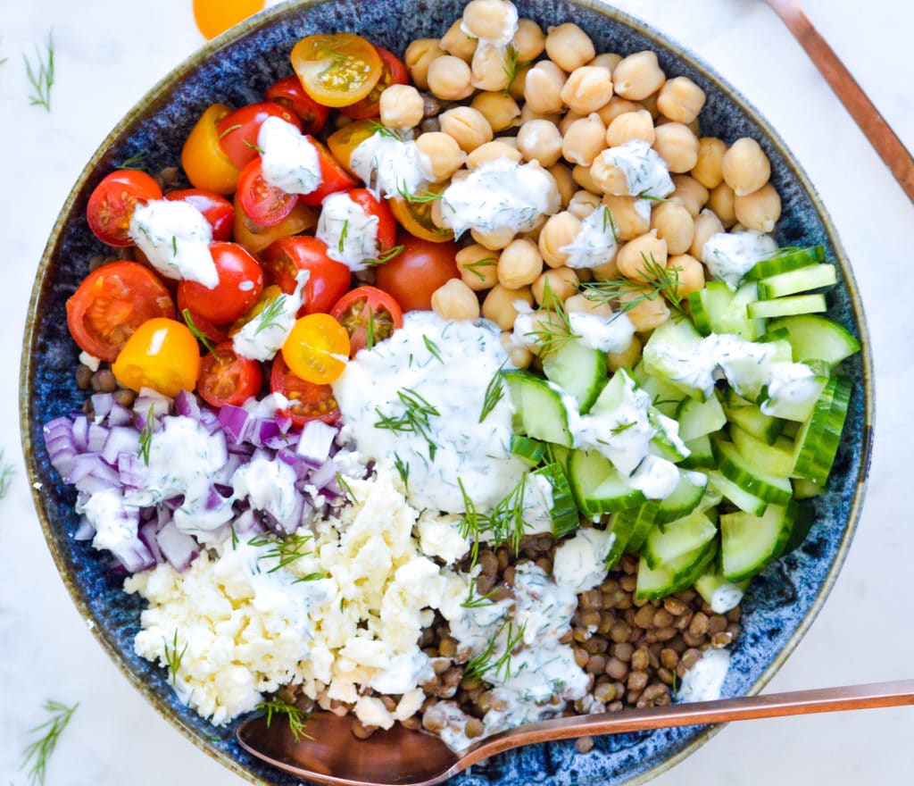 Greek lentil power bowl with chickpeas, cherry tomatoes, red onion, cucumber, feta and dill yogurt dressing