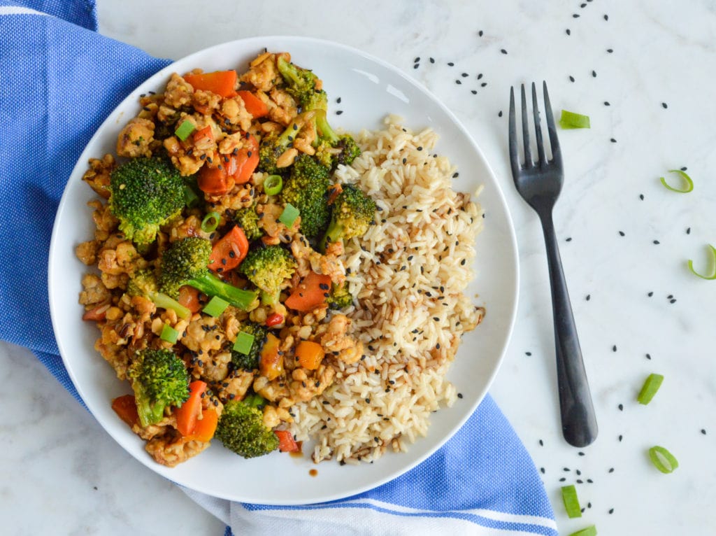 tempeh stir fry with brown rice on a white plate with black fork
